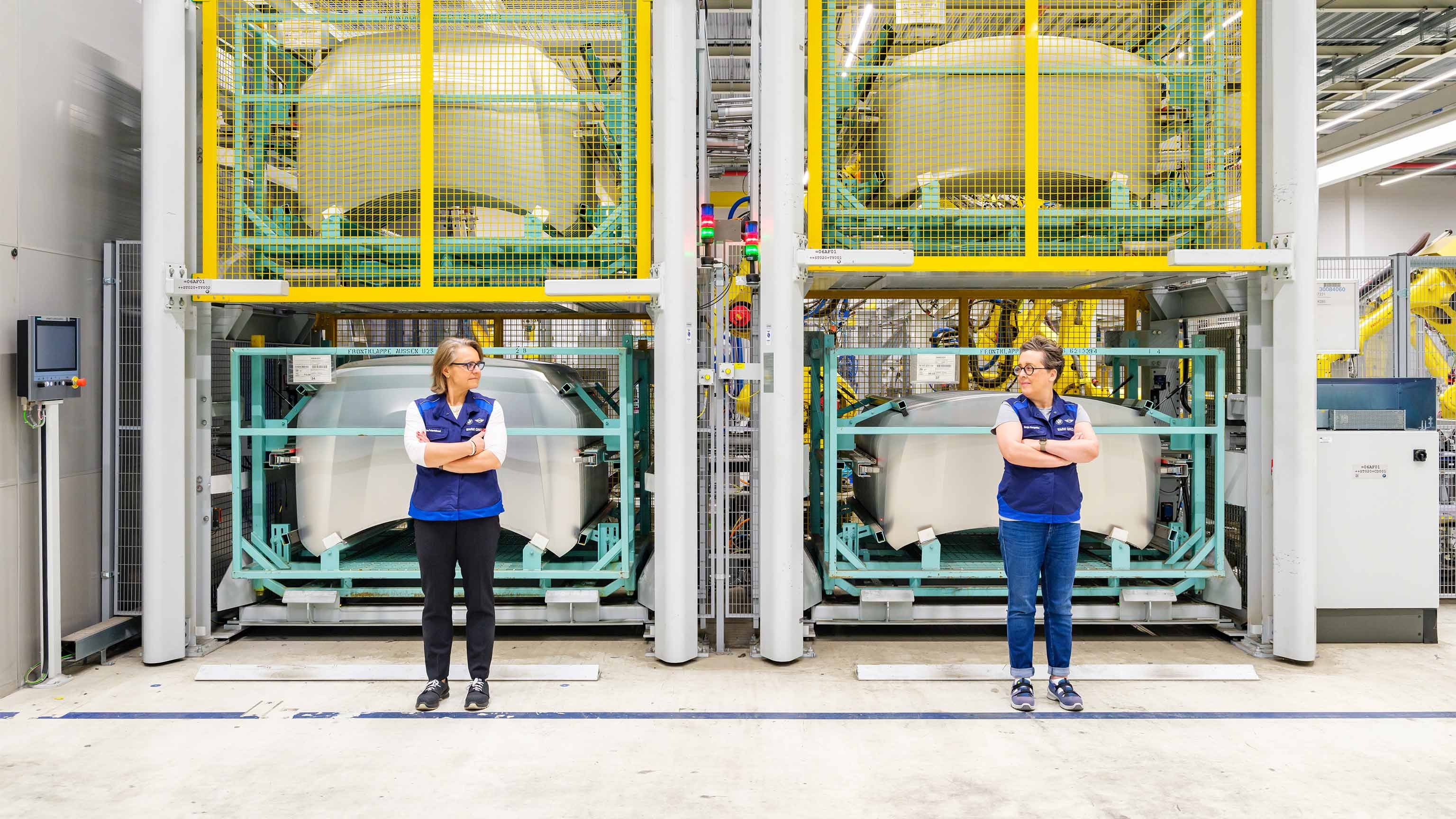 Arms crossed and wearing the plant’s mandatory vests, Plant Director and MINI Countryman Project Lead Sonja Hengstler share a glance as they stand in front of stored, unpainted car bonnets.